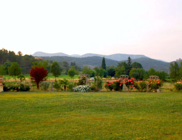 Vue panoramique du domaine Mas de Pradines avec pelouse, rosiers et montagnes de l'Hérault en fond