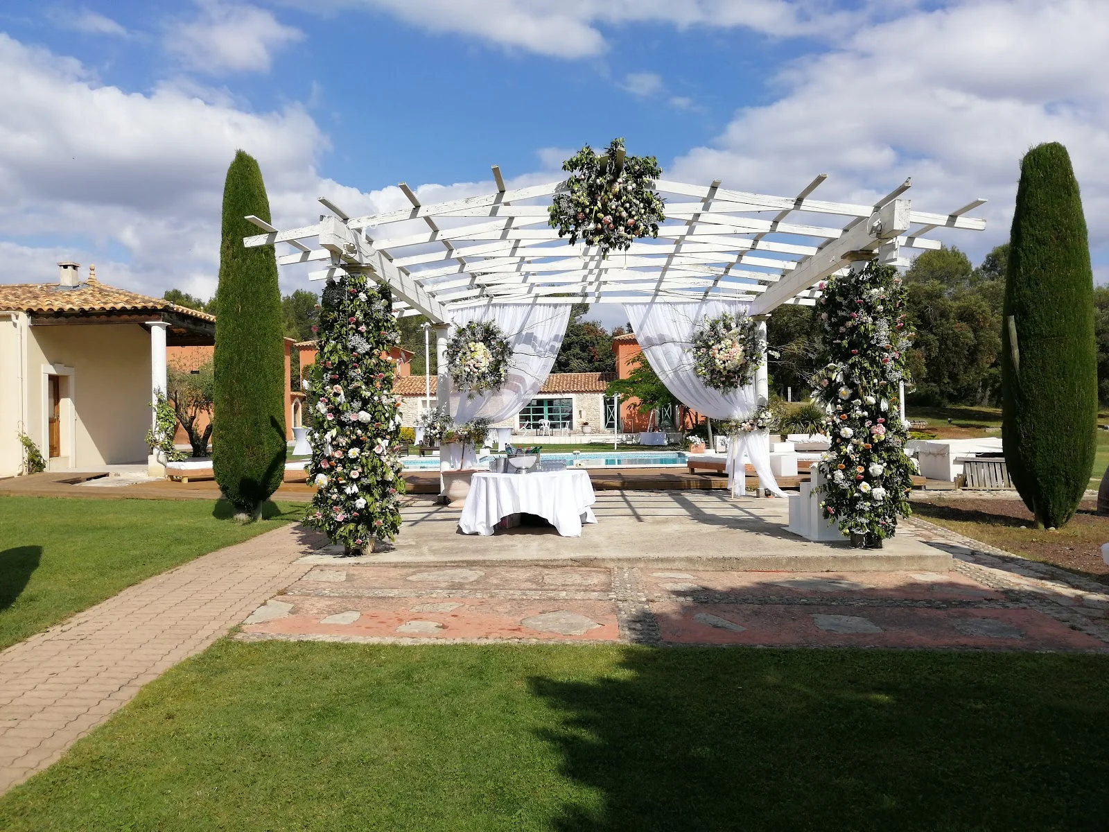 Cérémonie laïque sous pergola blanche décorée de fleurs et drapés au Mas Guilhem en Hérault