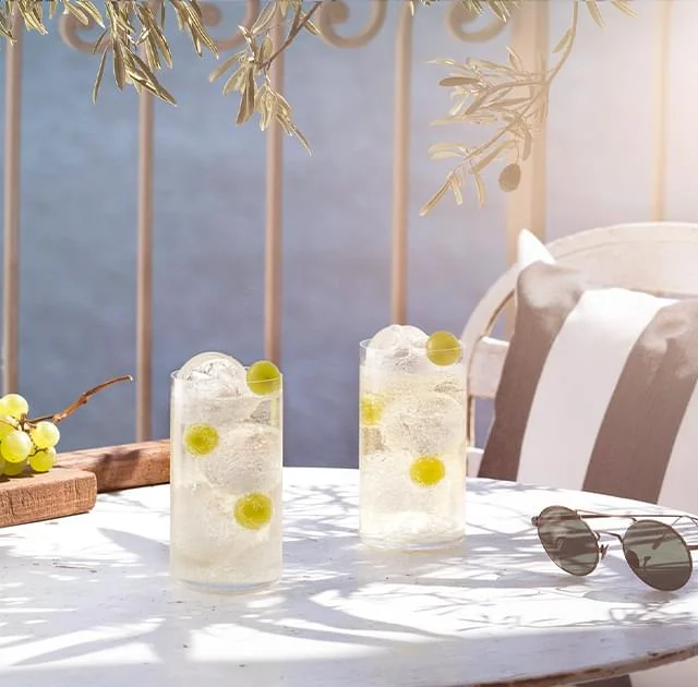 Deux cocktails Noilly Prat blanc avec raisins verts sur terrasse ensoleillée sous oliviers à Marseillan, Hérault