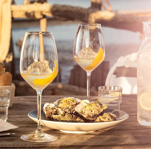 Verres de Noilly Prat blanc et plateau d'huîtres grillées sur table en bois face à l'étang de Thau à Marseillan, Hérault