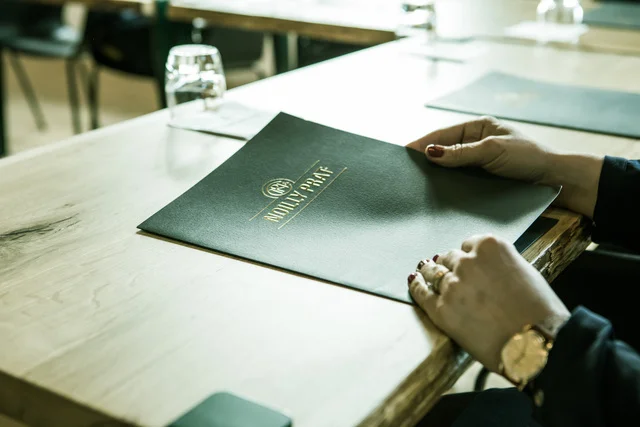 Menu en cuir noir Noilly Prat tenu par une femme dans la salle de réception à Marseillan, Hérault