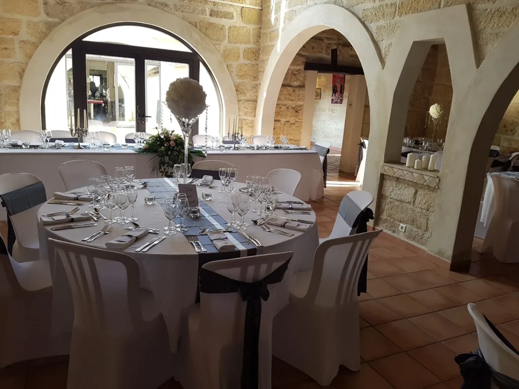 Salle voûtée en pierre aux tables rondes dressées pour un mariage à la Manade Occitane à Marsillargues