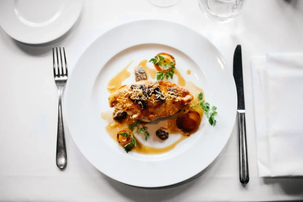 Plat principal nappé de sauce, garni de légumes et d’herbes, sur une assiette blanche — L’Atelier de Franck, traiteur de mariage à Colombiers