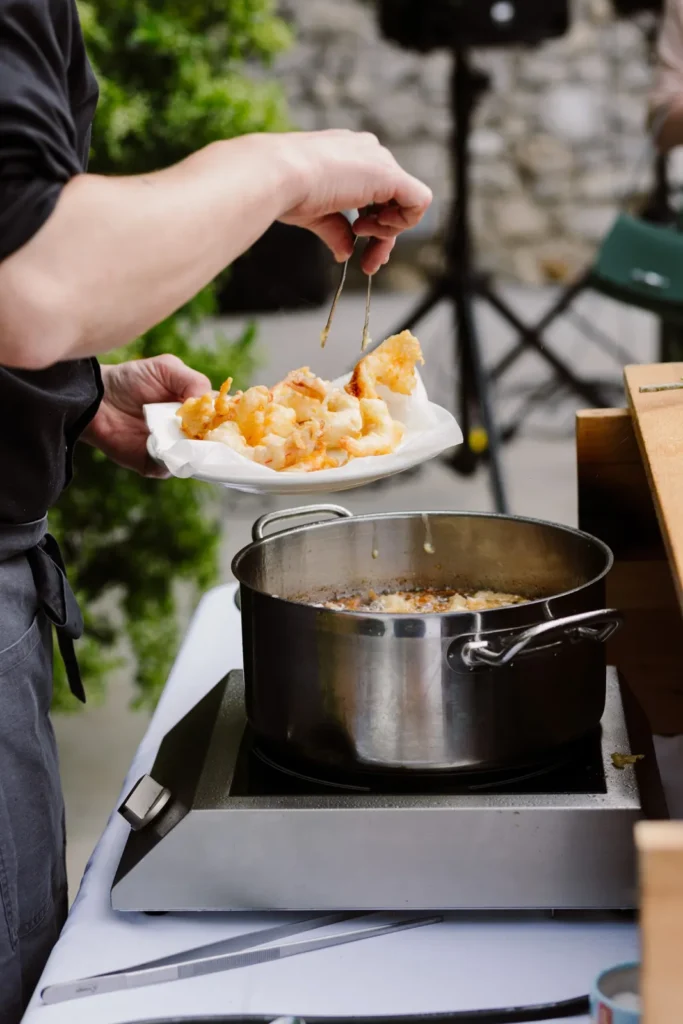 Chef égouttant des beignets dorés d’une assiette en papier au-dessus d’une marmite d’huile — Traiteur L’Évidence, Lattes
