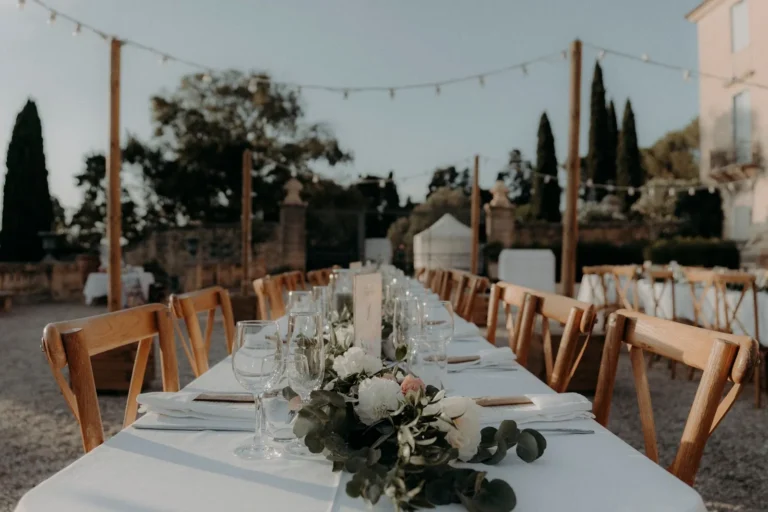 Longue table de réception de mariage dressée en extérieur avec nappe blanche et centres floraux — Traiteur L’Évidence, mariages à Lattes