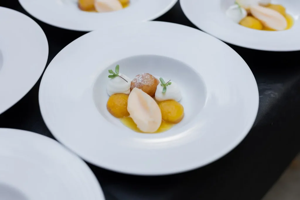 Dessert avec boules jaunes, fruit, beignet et crème fouettée sur une assiette blanche — La Petite Cuisine, traiteur de mariage à Manduel