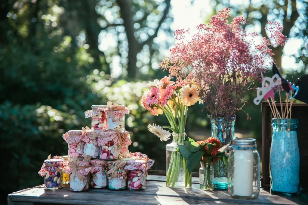Présentation de bonbonnières décorées et bouquets de fleurs sur une table en bois en extérieur — Husser Traiteur, Montpellier