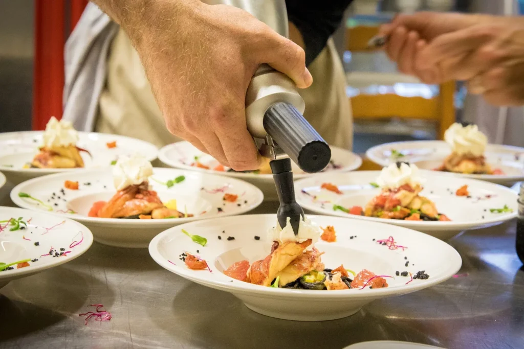 Un chef dépose une garniture crémeuse sur des assiettes en préparation pour un événement — Traiteur Grand, mariages à Montpellier