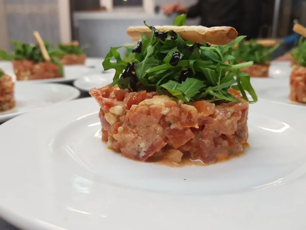 Tartare de tomates et feta garni de roquette et gressin sur une assiette blanche — À la Fourchette des Arènes, Nîmes