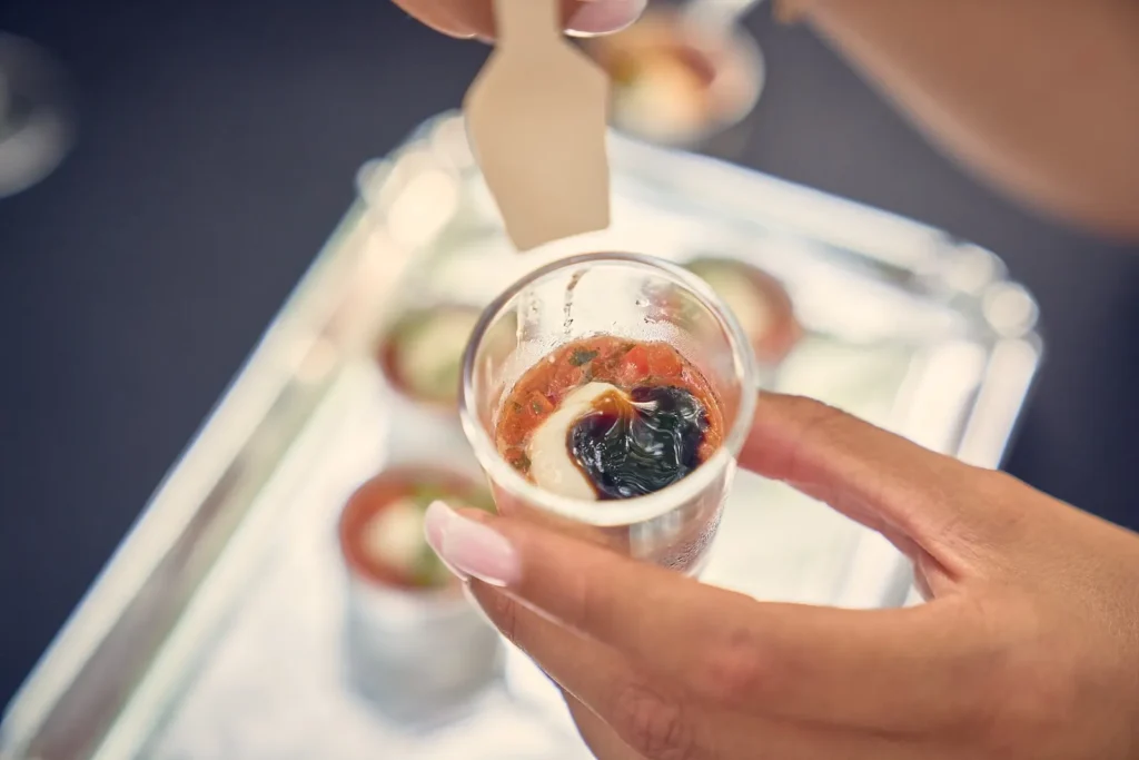 Main tenant une verrine d’amuse-bouche rouge et blanche, une autre main ajoute une sauce — La Cigale Traiteur, mariages à Nîmes