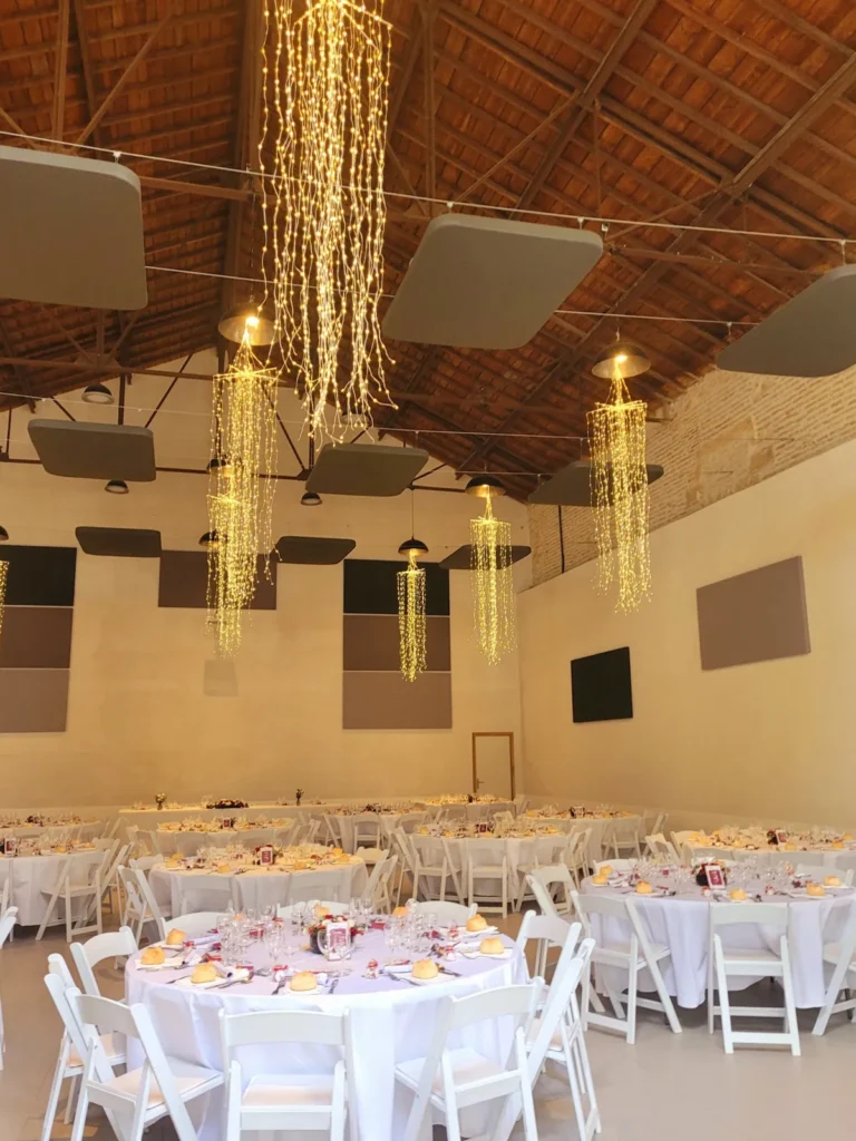 Vaste salle de réception avec tables rondes nappées de blanc et guirlandes lumineuses — L’Occitane Traiteur, Nîmes