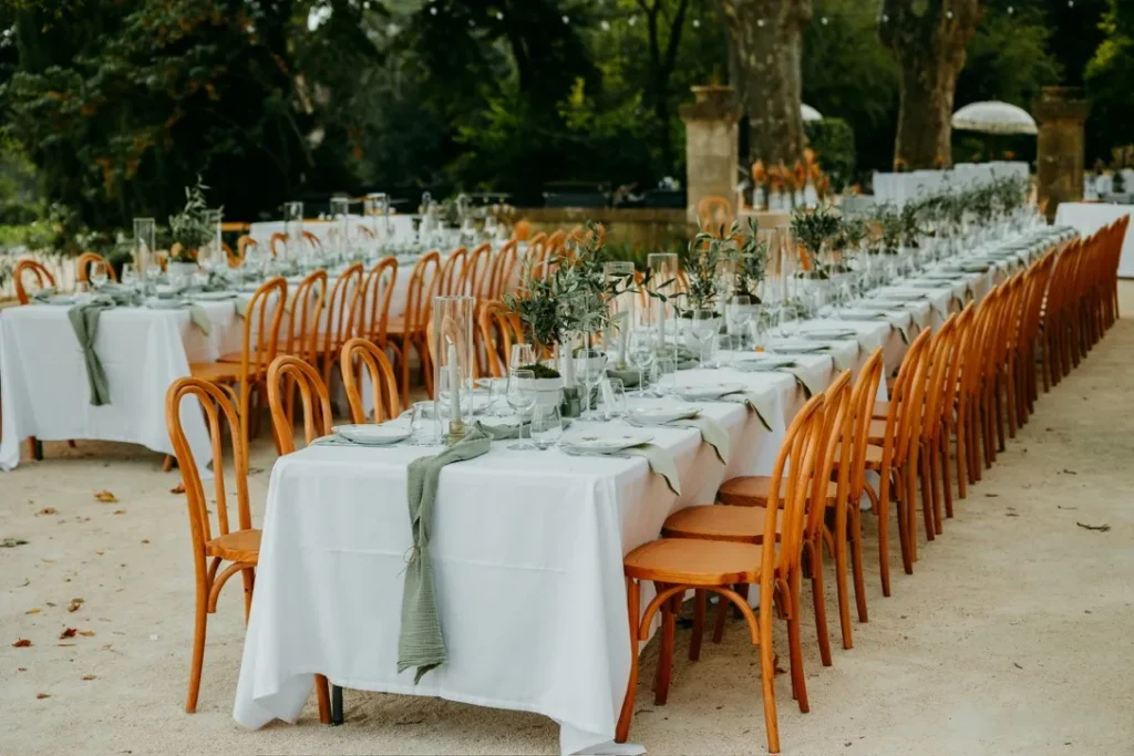 Longues tables de réception dressées en extérieur avec nappes blanches et serviettes vert sauge — Yello Event & Co, traiteur de mariage à Nîmes