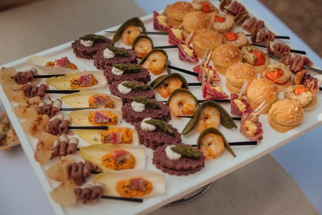 Grand plateau blanc de pièces cocktails salées avec brochettes de crevettes, mini-burgers et roulés — Traiteur Niguès, mariages à Peyriac-de-Mer