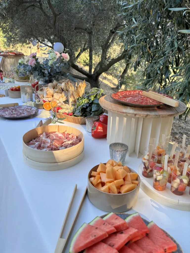 Buffet estival dressé en extérieur avec plateaux de charcuterie, salades et fruits frais coupés — Piadina Mia, traiteur de mariage à Portiragnes